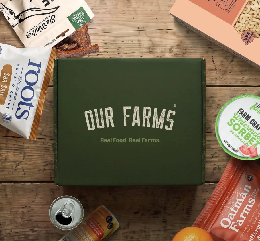 An Our Farms Box surrounded by farm snacks and mixes on a wood table
