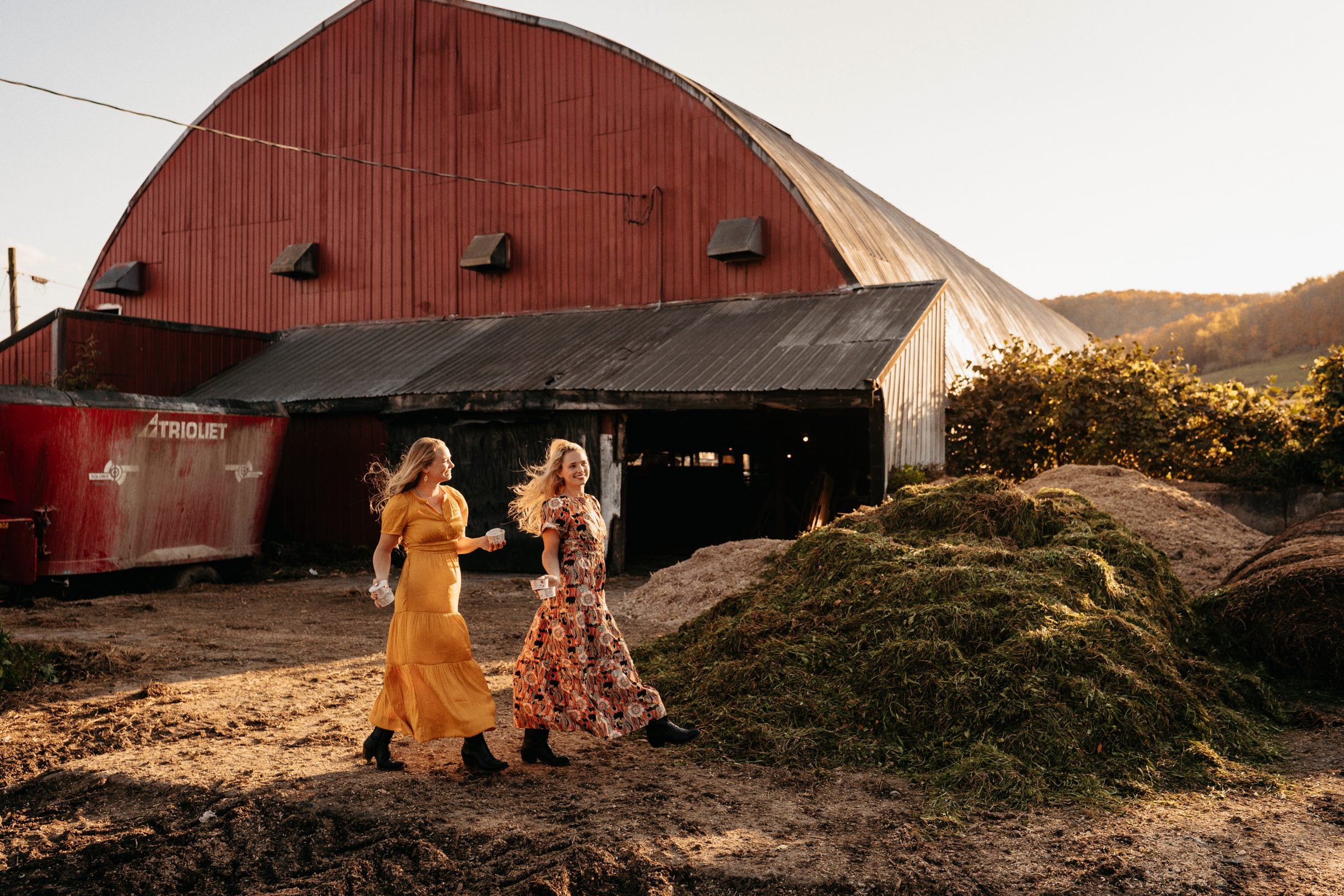 The Painterland sisters walking past the red barn on their family dairy farm, cups of yogurt in hand